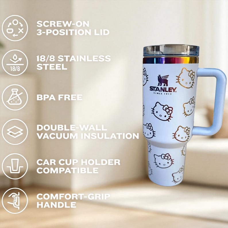 May include: A white Stanley travel mug featuring Hello Kitty graphics. The mug has a light blue handle and a screw-on lid. The text on the mug reads "STANLEY SINCE 1913". The mug is made of stainless steel and is car cup holder compatible.