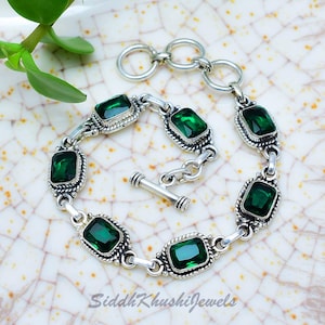 Puede incluir: Una pulsera de plata con piedras preciosas rectangulares de color verde esmeralda. La pulsera tiene un cierre de palanca y está compuesta por eslabones interconectados. Las piedras están engastadas en un marco de plata decorativo y texturizado. El texto "SiddhKhushiJewels" es visible.