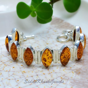 May include: A silver bracelet featuring multiple marquise-cut amber stones set in polished metal frames, connected by small cylindrical silver links, with a toggle clasp closure and the text SiddhKhushiJewels visible at the bottom.