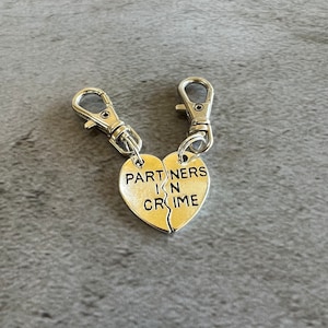 May include: Two silver keychains with split heart charms that read "Partners in Crime".