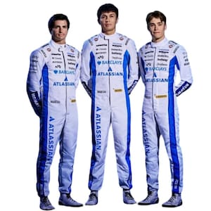 May include: Three people wearing white racing suits with blue accents and sponsor logos. The suits feature the "ATLASSIAN" logo prominently, along with "BARCLAYS" and "betway" branding. The suits have long sleeves and are zipped up.