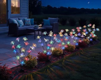 May include: A series of solar-powered garden lights shaped like fiber optic flowers, featuring thin stems and glowing, multi-colored petals in shades of blue, pink, green, and yellow, arranged in a row along a dark outdoor garden bed at night.
