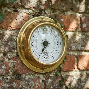 May include: A round tide clock with a polished brass frame and a white face. The dial features black markings, numbers one through five, and the text "TIDE CLOCK," "HIGH TIDE," "LOW TIDE," "RISING TIDE," and "FALLING TIDE" with a ship graphic.