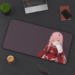 May include: A rectangular mousepad with a dark purple surface and a cartoon image of a female anime character with pink hair and red clothing. A white computer mouse is on the right side of the mousepad.