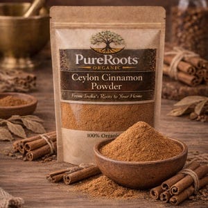 May include: A package of PureRoots Organic Ceylon Cinnamon Powder, with the text "From India's Roots to Your Home". A wooden bowl contains a pile of cinnamon powder, and cinnamon sticks are arranged around it. The image is set on a wooden surface.