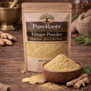 May include: A packet of PureRoots Organic Ginger Powder is displayed alongside a wooden bowl filled with ginger powder. Sliced ginger and ginger roots are also visible. The packaging reads "From India's Roots to Your Home."