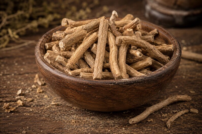 May include: A wooden bowl filled with dried, light brown, stick-like pieces, possibly herbs or roots. The bowl sits on a wooden surface, with some of the pieces scattered around it. The image has a warm, natural tone, suggesting a focus on organic products.