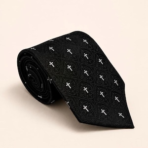 Può includere: Una cravatta nera con un motivo ripetuto di piccole croci bianche. Il tessuto presenta una sottile trama jacquard tono su tono con un intricato motivo a forma di diamante che conferisce un aspetto strutturato all'intera superficie.