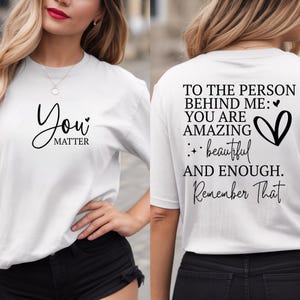 May include: White t-shirt with black text. The front says "You Matter" in a script font. The back of the shirt has the message "To the person behind me: You are amazing, beautiful and enough. Remember That."