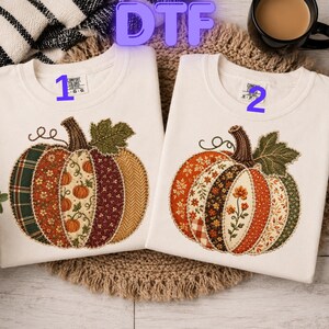 May include: Two white t-shirts featuring a large pumpkin graphic on the front. The pumpkin is composed of various fabric-like patterns in shades of orange, green, brown, and cream. The shirts are labeled with the numbers 1 and 2 in blue text.