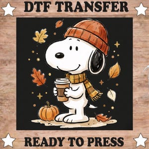 May include: A DTF transfer ready to press featuring a white cartoon dog wearing an orange knit beanie and a matching striped scarf. The dog holds a brown coffee cup, surrounded by orange and yellow autumn leaves, a pumpkin, and stars on a black background.