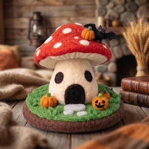 May include: A needle-felted mushroom house sculpture featuring a red cap with white spots, a cream-colored stem with a black arched door and two windows, sitting on a green base with small orange pumpkins and a black bat perched on top.