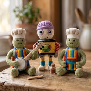 Pode incluir: Duas criaturas verdes de feltro com gorros de chef brancos e aventais às riscas arco-íris, uma delas a segurar um pequeno banjo, ao lado de um robô central de feltro com gorro roxo, torso amarelo com ícone de azeitona e um frasco.