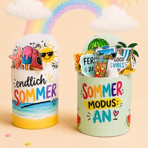 Può includere: Due contenitori cilindrici in carta decorati con temi estivi. Il contenitore a sinistra presenta una scena di spiaggia con il testo "endlich SOMMER". Quello a destra mostra fette di anguria e il testo "SOMMER MODUS: AN" con vari ritagli a tema estivo.