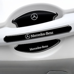 May include: A white ceramic mug with a black handle and the text "But First, Coffee" in a black, handwritten-style font. The mug is on a white surface.