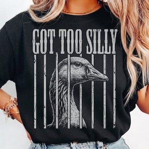 May include: Black t-shirt with the text "GOT TOO SILLY" above a grayscale illustration of a goose behind bars. The goose's head and neck are visible, with the bars creating a caged effect. The shirt is a crew neck.