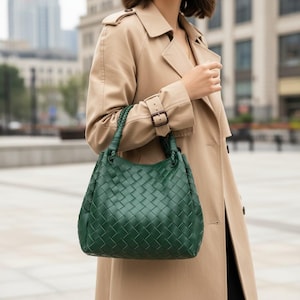 Peut inclure: Un sac &agrave; main vert fonc&eacute; pr&eacute;sentant un motif en cuir tress&eacute; sur toute la surface ext&eacute;rieure. Le sac est dot&eacute; de deux anses tress&eacute;es fix&eacute;es sur le dessus, lui conf&eacute;rant une forme structur&eacute;e. La texture est uniforme et quadrill&eacute;e.