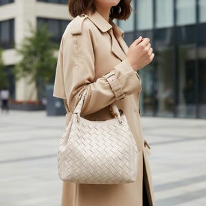 Peut inclure: Un sac &agrave; main en cuir de couleur cr&egrave;me pr&eacute;sentant un motif tress&eacute; complexe sur tout l'ext&eacute;rieur. Le sac poss&egrave;de une base structur&eacute;e, une poign&eacute;e sup&eacute;rieure unique avec des d&eacute;tails tress&eacute;s et des ferrures dor&eacute;es reliant la poign&eacute;e au corps.