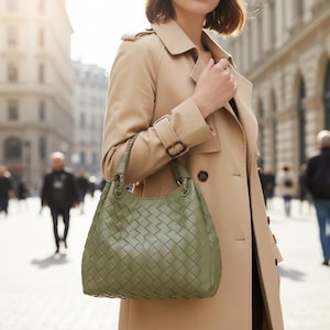Peut inclure: Un sac hobo vert olive dot&eacute; d'un motif en cuir tress&eacute; complexe et d'une anse tress&eacute;e. Le sac pr&eacute;sente une base structur&eacute;e et une silhouette souple, avec des &eacute;l&eacute;ments m&eacute;talliques reliant l'anse au corps principal du sac &agrave; main.