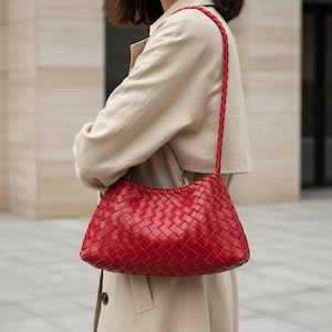 Pode incluir: Uma bolsa de ombro de couro vermelho tecido com uma al&ccedil;a tran&ccedil;ada. A bolsa tem formato retangular com bordas arredondadas. A bolsa &eacute; carregada no ombro. A bolsa &eacute; de cor vermelha vibrante.