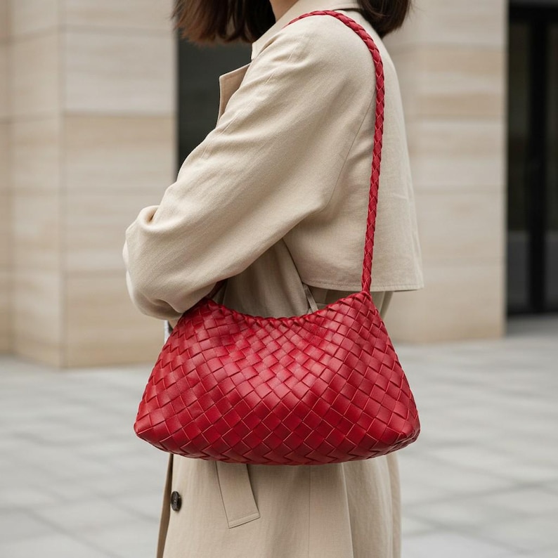Pode incluir: Uma bolsa de ombro de couro vermelho tecido com uma al&ccedil;a tran&ccedil;ada. A bolsa tem formato retangular com bordas arredondadas. A bolsa &eacute; carregada no ombro. A bolsa &eacute; de cor vermelha vibrante.