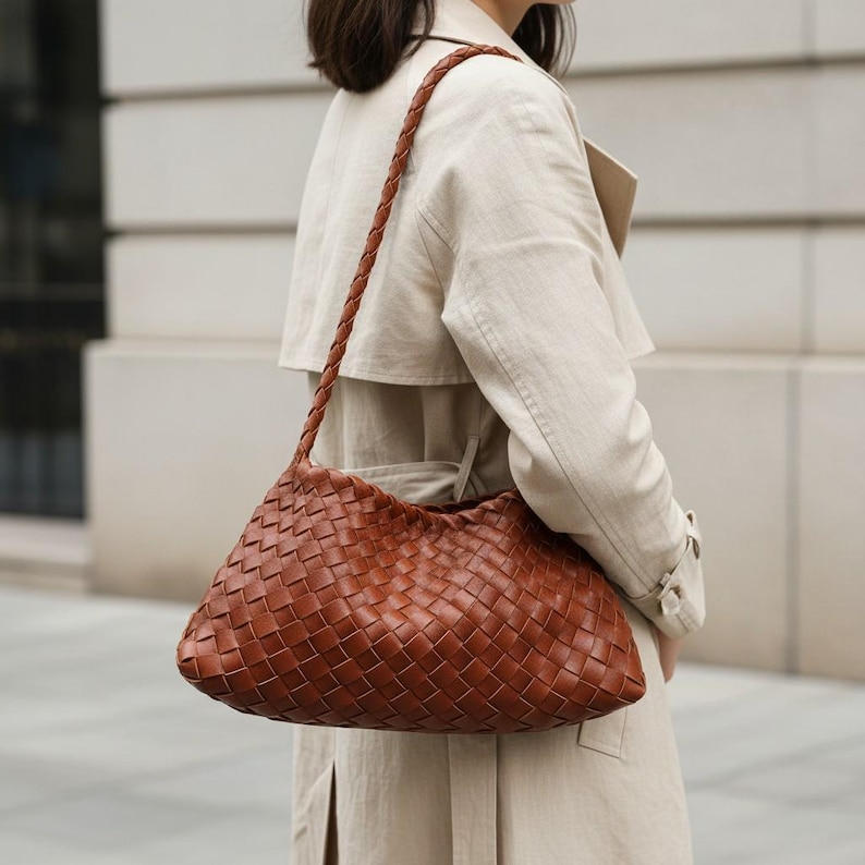 Pode incluir: Uma bolsa de ombro de couro tran&ccedil;ado marrom com uma al&ccedil;a tran&ccedil;ada. A bolsa tem formato triangular e &eacute; usada no ombro. A bolsa &eacute; feita de couro marrom quente.