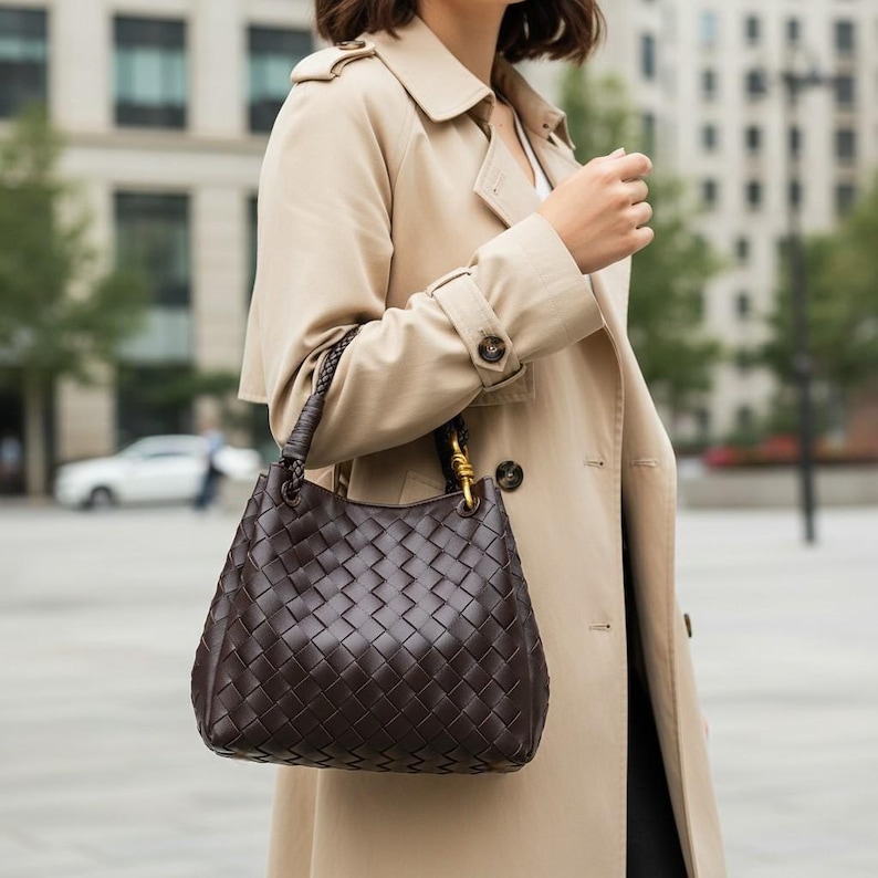 Peut inclure: Un sac &agrave; main marron fonc&eacute; dot&eacute; d'un motif en cuir tress&eacute; complexe. Le sac pr&eacute;sente une base arrondie structur&eacute;e et une poign&eacute;e tress&eacute;e unique fix&eacute;e au corps par des &eacute;l&eacute;ments m&eacute;talliques dor&eacute;s, assurant une prise en main pratique.