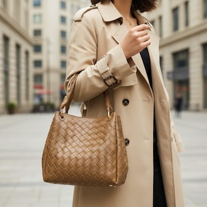 Peut inclure: Un sac &agrave; main marron de taille moyenne pr&eacute;sentant un motif en cuir tress&eacute; complexe sur tout l'ext&eacute;rieur. Le sac comprend deux anses en cuir tress&eacute; fix&eacute;es par des &eacute;l&eacute;ments m&eacute;talliques dor&eacute;s et une base structur&eacute;e avec de petits pieds.