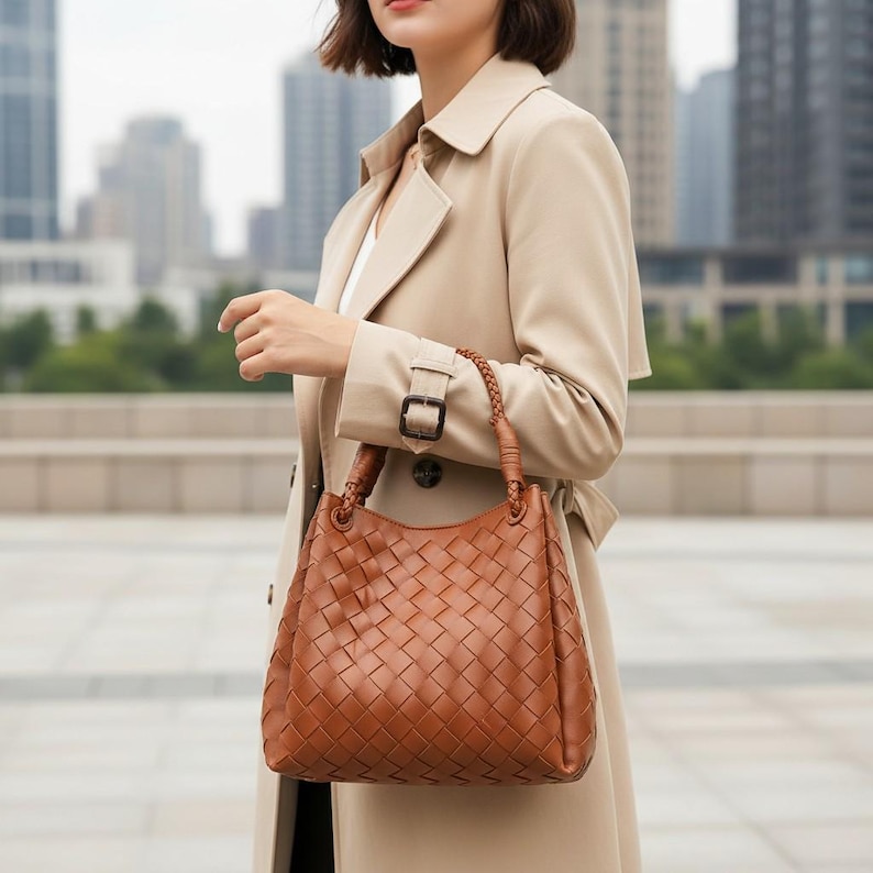 Peut inclure: Un sac &agrave; main de couleur brun cognac de taille moyenne pr&eacute;sentant un motif en cuir tress&eacute; complexe sur tout l'ext&eacute;rieur. Le sac a une forme hobo structur&eacute;e avec une seule poign&eacute;e en cuir tress&eacute; fix&eacute;e au sommet par des anneaux m&eacute;talliques.