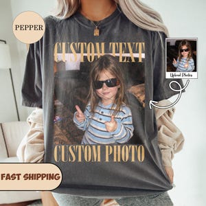 May include: A charcoal gray short-sleeve t-shirt featuring a large rectangular graphic print of a child wearing sunglasses and a blue striped shirt, with the text CUSTOM TEXT above and CUSTOM PHOTO below the image in a bold tan serif font.