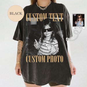 May include: A black short-sleeve t-shirt featuring a large central graphic of a child wearing sunglasses and giving a thumbs up. The text CUSTOM TEXT appears above the image and CUSTOM PHOTO appears below in a tan serif font. A small circle says BLACK.