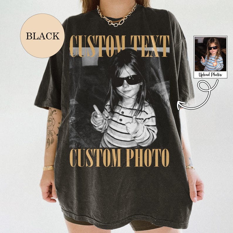 May include: A black short-sleeve t-shirt featuring a large central graphic of a child wearing sunglasses and giving a thumbs up. The text CUSTOM TEXT appears above the image and CUSTOM PHOTO appears below in a tan serif font. A small circle says BLACK.