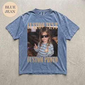 May include: A blue jean colored short-sleeve t-shirt featuring a rectangular graphic print of a child wearing sunglasses and a striped shirt, making hand gestures. The text CUSTOM TEXT appears above the photo and CUSTOM PHOTO below it.