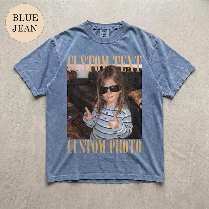 May include: A blue jean colored short-sleeve t-shirt featuring a rectangular graphic print of a child wearing sunglasses and a striped shirt, making hand gestures. The text CUSTOM TEXT appears above the photo and CUSTOM PHOTO below it.