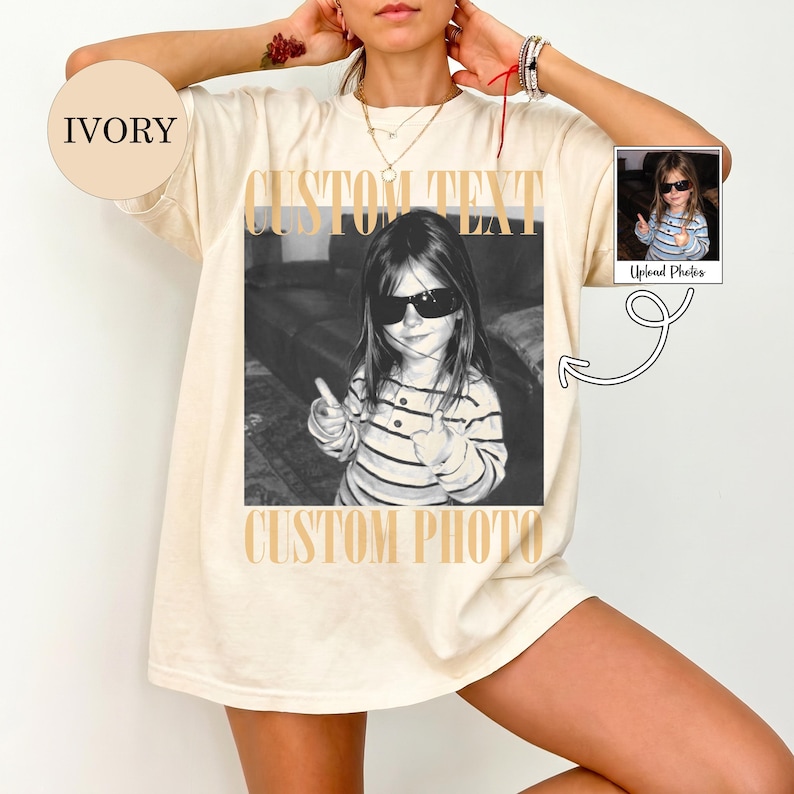 May include: An ivory t-shirt featuring a large black and white graphic print of a child wearing sunglasses and giving a thumbs up. The text CUSTOM TEXT appears above the photo and CUSTOM PHOTO appears below it. A small circular ivory tag reads IVORY.