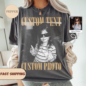 May include: A charcoal gray short-sleeve t-shirt featuring a black and white photograph of a child wearing sunglasses and giving a thumbs up. The text CUSTOM TEXT appears in tan above the photo, and CUSTOM PHOTO appears in tan below the photo.