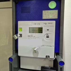 Könnte beinhalten: Ein Stromzähler mit digitaler Anzeige, weiß mit blau-grauem Rahmen. Die Anzeige zeigt den Energieverbrauch in kWh an. Auf dem Zähler steht "Landis, E360-3P".
