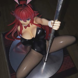 May include: A figurine of a woman in a black bunny suit, fishnet stockings, and pink bunny ears. The figure has red hair and is holding a silver pole. The figurine is on a silver base.