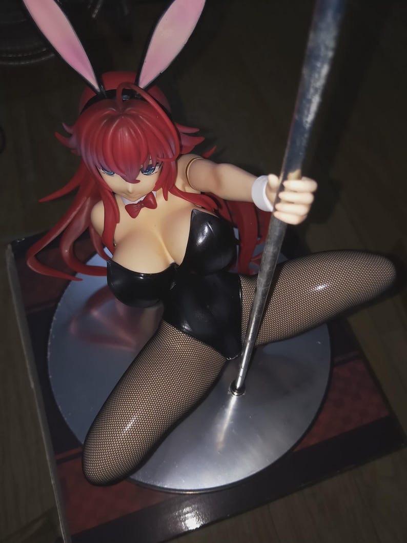 May include: A figurine of a woman in a black bunny suit, fishnet stockings, and pink bunny ears. The figure has red hair and is holding a silver pole. The figurine is on a silver base.