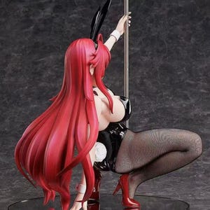 May include: A figurine of a woman in a black bunny outfit, red heels, and fishnet stockings, holding onto a silver pole. The figure has long red hair and black bunny ears.