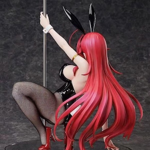 May include: A figurine of a person in a black bunny suit, fishnet stockings, and red high heels, posed with one arm raised holding a pole. The figure has long, flowing red hair and black bunny ears.