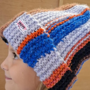 Könnte beinhalten: Eine grob gestrickte Mütze mit horizontalen Streifen in Hellblau, leuchtendem Orange, Dunkelblau und Braun. Ein weißes, rechteckiges Stoffetikett mit dem schwarzen Schriftzug AROYO ist an der Vorderseite des umgeschlagenen Saums befestigt.