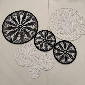 May include: A collection of handmade, circular doilies in various sizes and designs. The doilies are in black and white, with intricate openwork patterns. The arrangement includes both solid and open designs, creating a visually appealing contrast.