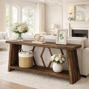 May include: A dark brown wooden console table with a lower shelf and angled legs. The table is decorated with a white vase of flowers, a framed picture, and a gold decorative object. A woven basket with a white liner sits on the lower shelf.