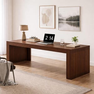 May include: A dark brown wooden desk with a rectangular design. A laptop displays the time 2:14. The desk is accessorized with a lamp, books, a glass of water, and a small plant. Two framed pictures hang on the wall behind the desk.