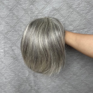 May include: A short, layered hairpiece featuring a blend of silver, gray, and dark charcoal tones. The hair is styled with a smooth, straight texture, showcasing natural-looking highlights and lowlights throughout the strands for depth and dimension.