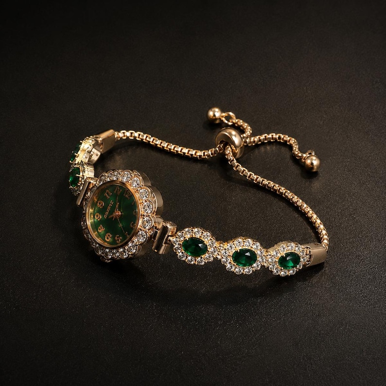 May include: A gold-tone bracelet watch featuring a round green dial with gold numerals, surrounded by a halo of clear crystals. The band consists of a box chain with three oval green stones set in crystal-encrusted frames and an adjustable slider.