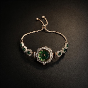 May include: A gold-tone bracelet watch featuring a round, emerald green dial surrounded by a floral-shaped bezel set with clear crystals. The band consists of alternating clear crystal and emerald green stone links with an adjustable sliding clasp.
