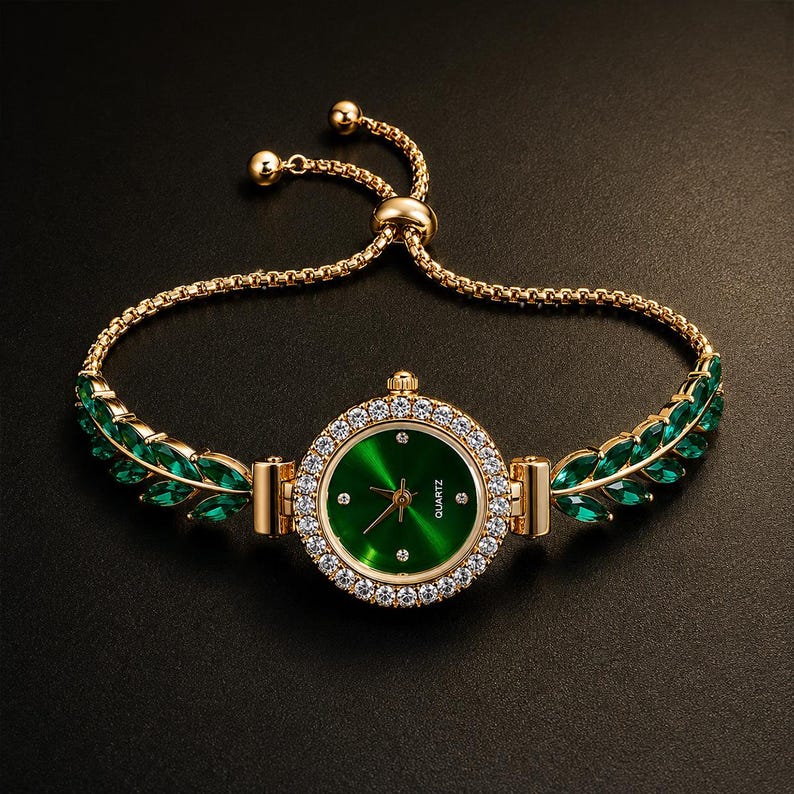 May include: A gold-tone quartz watch with a round green face and a bezel set with clear crystals. The watch band features a gold chain with green leaf-shaped stones on each side and an adjustable sliding clasp mechanism for a secure fit.