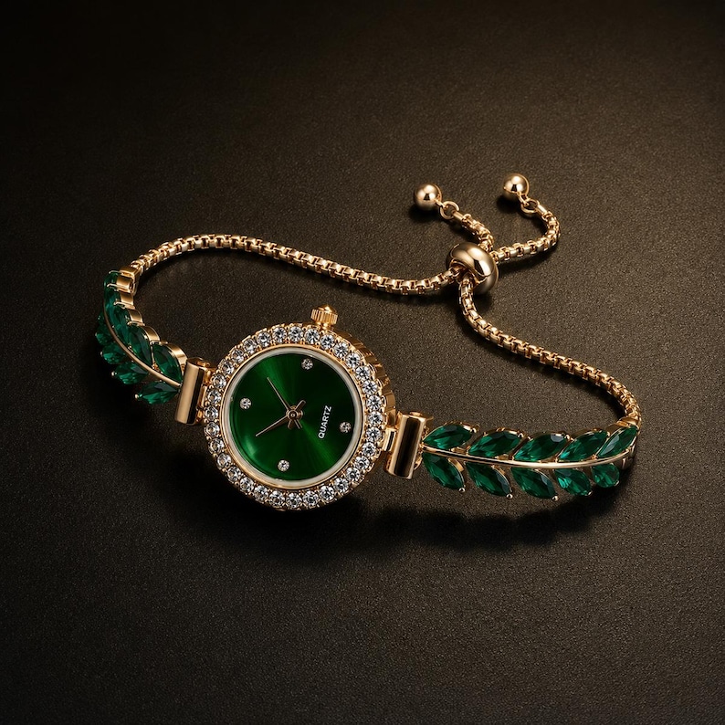 May include: A gold-tone quartz watch featuring a round green dial with small crystal hour markers. The bezel is encrusted with clear stones. The bracelet consists of gold-tone chains adorned with marquise-cut green leaves and an adjustable slider.